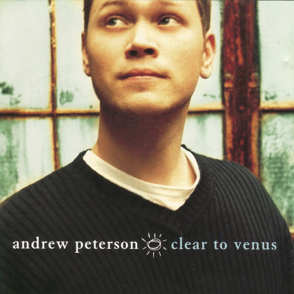 Album Art of Andrew Peterson's Clear To Venus album - A close-up photo of a young, clean-shaven man with brown hair wearing a white T-shirt under a dark green sweater. The top of his head is cut off at the top of the frame, and behind him can be seen a door with painted pieces of glass that cannot be seen through. Towards the bottom, printed on top of his sweater, is the artist's name in lowercase white text on the left in white and the album title on the right in aqua blue-green. In between is a drawing of sun that is a couple rough circles surrounded by lines radiating from it.