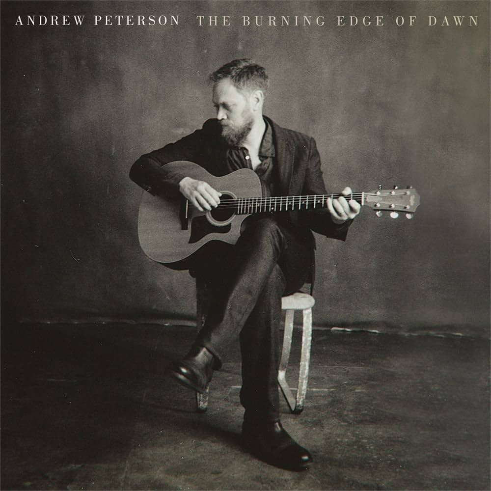 Album Art of Andrew Peterson's The Burning Edge of Dawn album - In what looks like a photography studio with a generic floor and background, a middle-aged white man with a beard sits on a stool playing a guitar and looking down and off to their right. The photo is back-and-white. Across the top it has the artist name and title in a small font.