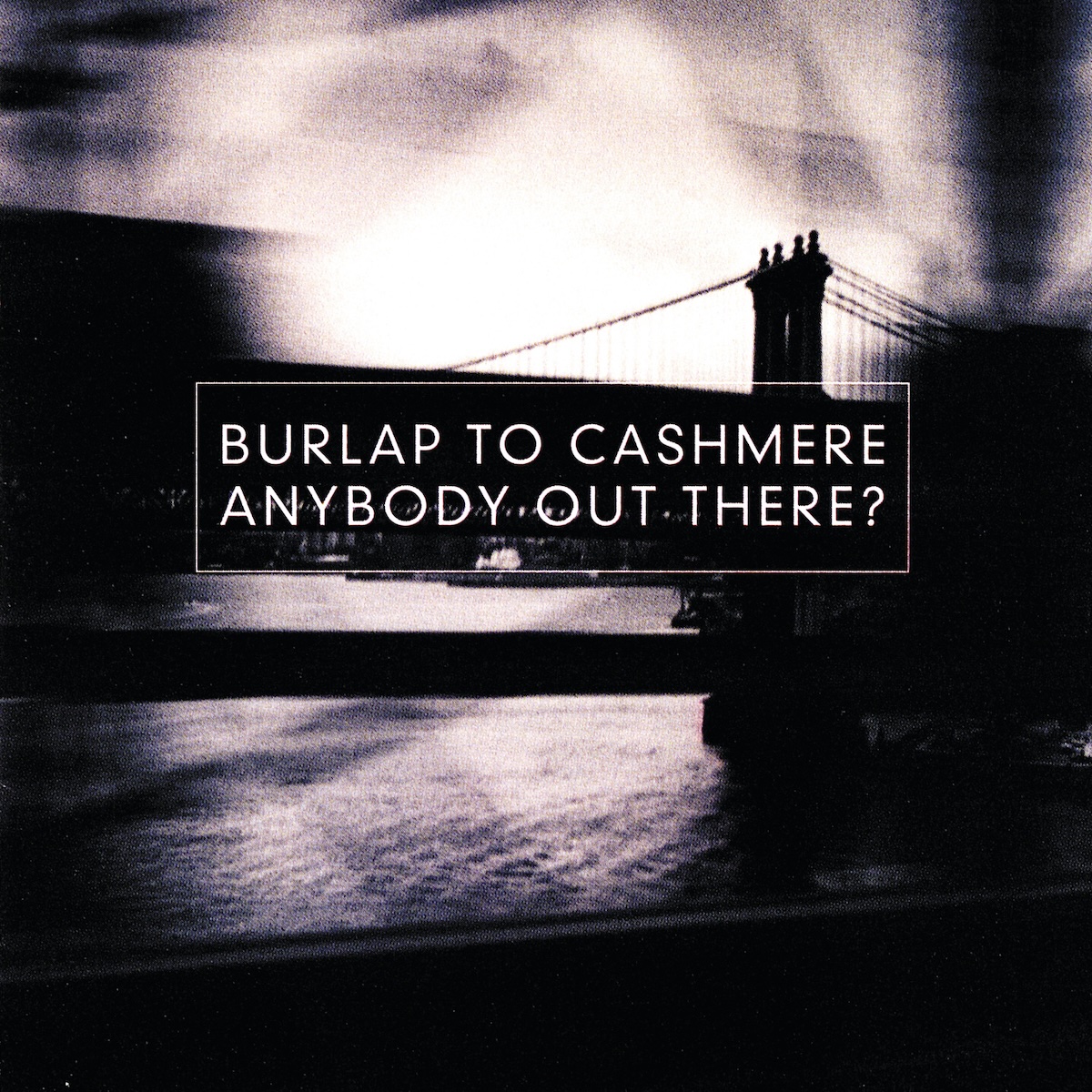 Album Art of Burlap To Cashmere's Anybody Out There? album - A grainy black-and-white photo with lots of motion blur that looks like it was taken from a moving vehicle on a bridge. In the foreground there are a bunch of barriers on the bridge that are silhouetted against the water and sky beyond them. The huge structure of a tower of a nearby bridge, maybe the Brooklyn Bridge, with cables coming of each side of the top, can be seen clearly, with a deck below that and the buildings being covered by some writing so harder to make out. In the center, there's a white outline of a rectangle, and inside that it has the band's name on one line and the album title on a line below it, both the same size white text.