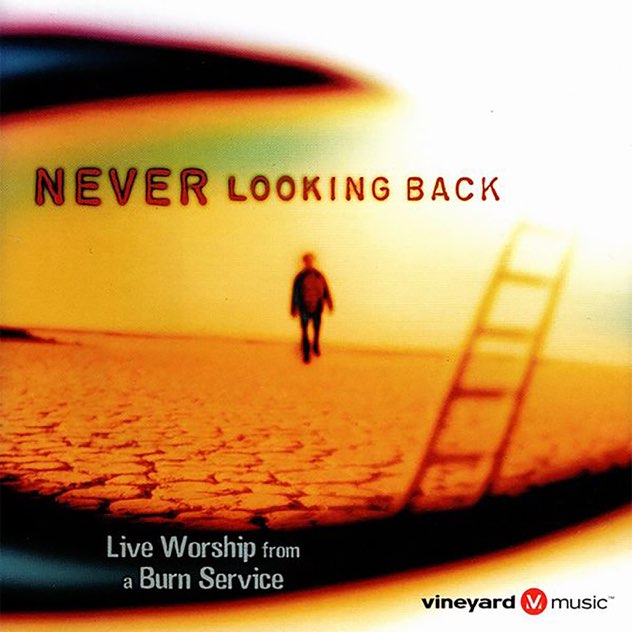 Album Art of The Burn Service's Never Looking Back album - Through some sort of blurry lens, we see a person walking through a very cracked desert landscape. In the blurry foreground, there seems to be a ladder. The title above the person is 'Never Looking Back', and in smaller print below the photo it says 'Live worship from a burn service' and in the bottom right is the 'Vineyard Music' logo.