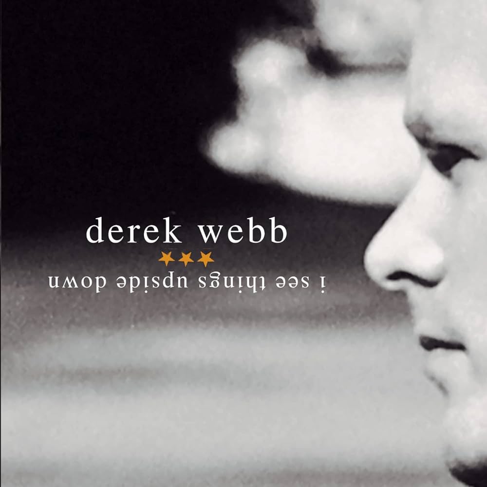 Album Art of Derek Webb's I See Things Upside Down album - A black and white photo that has, on the right, a profile of Derek Webb's face and the rest of the background is filled with what looks like an out-of-focus sky and clouds. On that background is written in lowercase white print the artist name and the album title, separated by three gold stars.