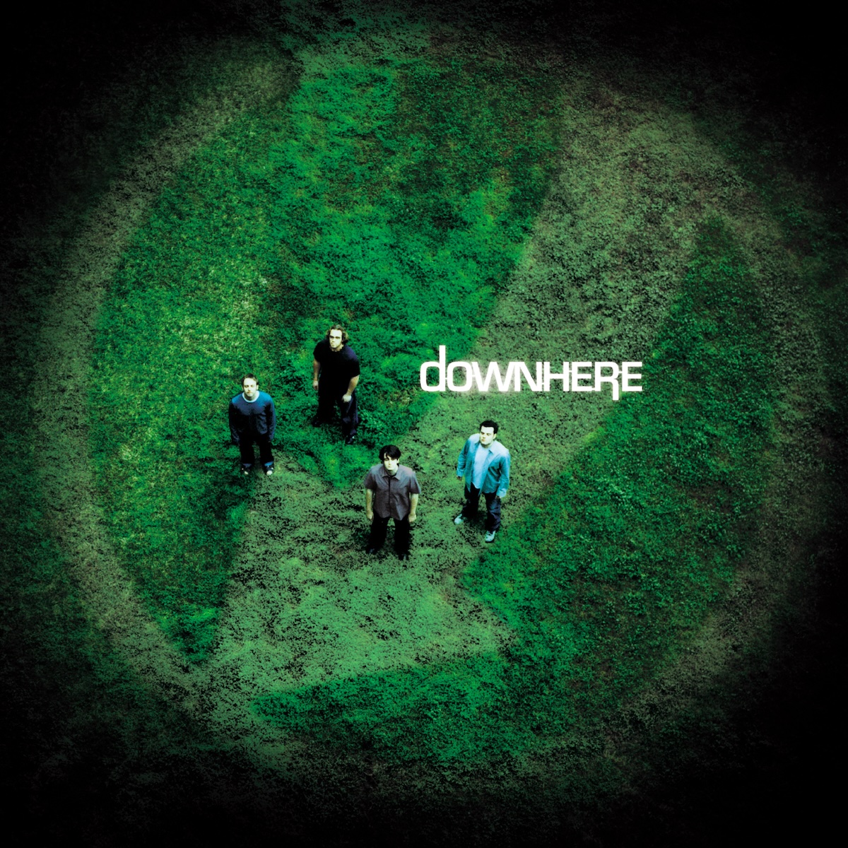 Album Art of Downherel's self-titled album - From way up in the air above, four men are photographed in a grassy field. They are standing apart and looking up towards the camera. The edges of the photo fade to black in a circle. Printed on top of the photo in the middle just to the right and above the band members is the band's name in mostly uppercase white text, though the first letter 'D' is lowercase and taller as well as the 'R' extends below all other letters on the right.