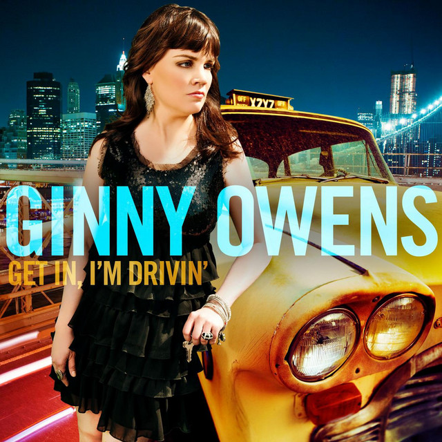 Album Art of Ginny Owens's Get In, I'm Drivin' album - A photo of the New York City skyline taken from the Brooklyn Bridge with cars streaking by on the deck below is the background. On top of that is layered a woman with brown hair down past her shoulders, bangs and a frilly black dress leaning on a classic yellow cab that looks a bit worn out. She's got a bunch of jewelry on her fingers and wrists and keys in her left hand. Printed over the top of these in big, semi-transparent aqua blue letters is the artist's name right in the center, with the album title in smaller, yellow letters just below it to the left.