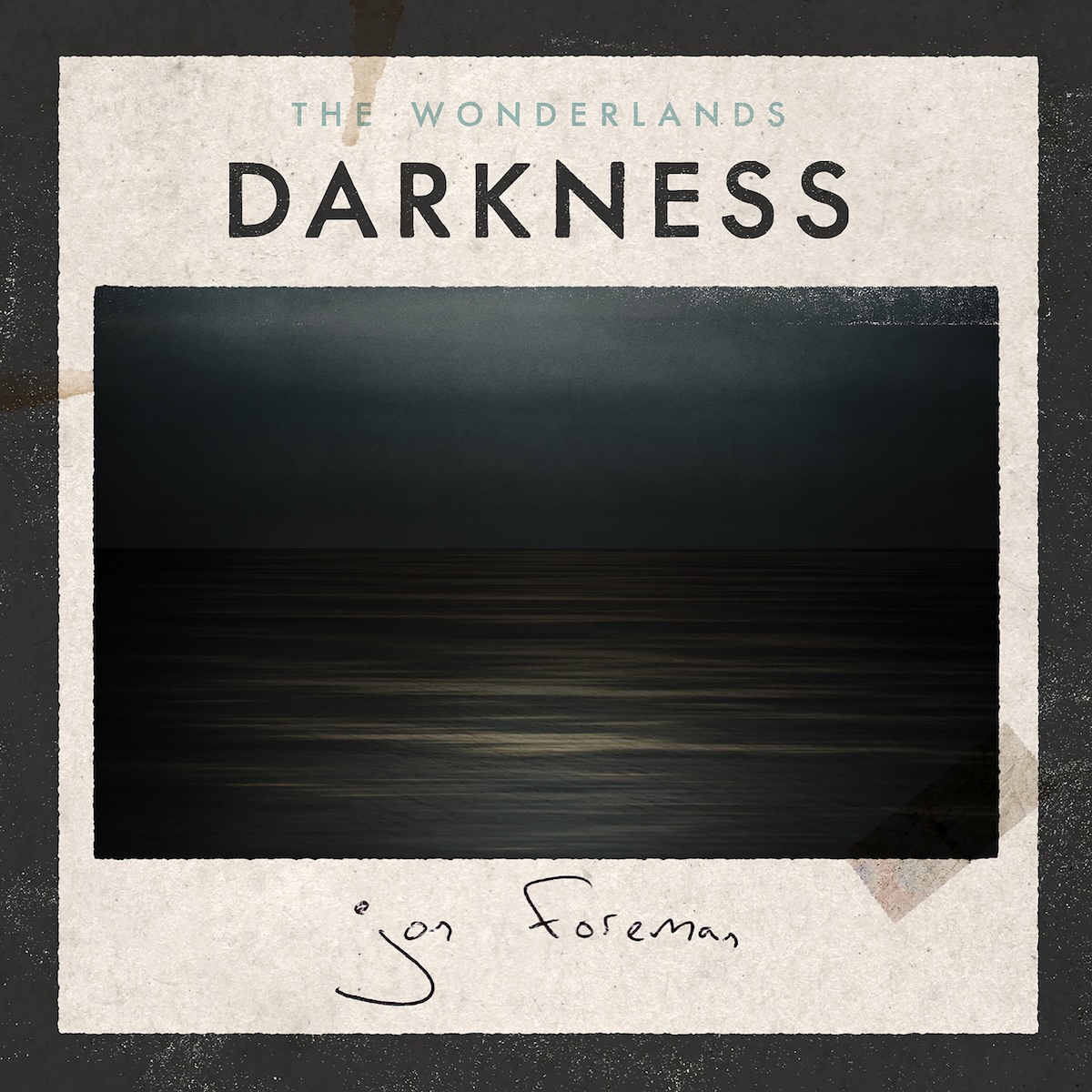  Darkness EP - On what looks like rough, light brown paper with a coffee cup stain in the top left, there is a photo of a black sky with a with some potential clouds over a calm, wide body of black water. On the top right edge, the image is worn out a bit, and there's a piece of clear tape on the bottom right of the image, affixing it to the paper. Above it, in the middle, it says 'The Wonderlands' in a smaller, light gray font, and 'Darkness' in a much larger black text. Below the photo, there's a handwritten, thin pen signature of Jon Foreman. There's also a thick black border around it.