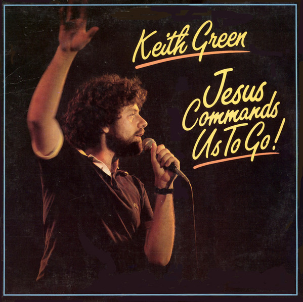 Album Art of Keith Green's Jesus Commands Us To Go! album - On a dark stage, a color photo of a young man with a short beard and couple-inch-long, curly brown hair is holding a microphone up to his mouth in one hand with his other hand lifted off to the right, maybe in a teaching motion. He's wearing a dark red polo shirt. Written to the right of him in a yellow script-like font is the artist's name and below that, the album title. Both of them have an orange underline below them too. There's also a thin, light blue border around the edge.