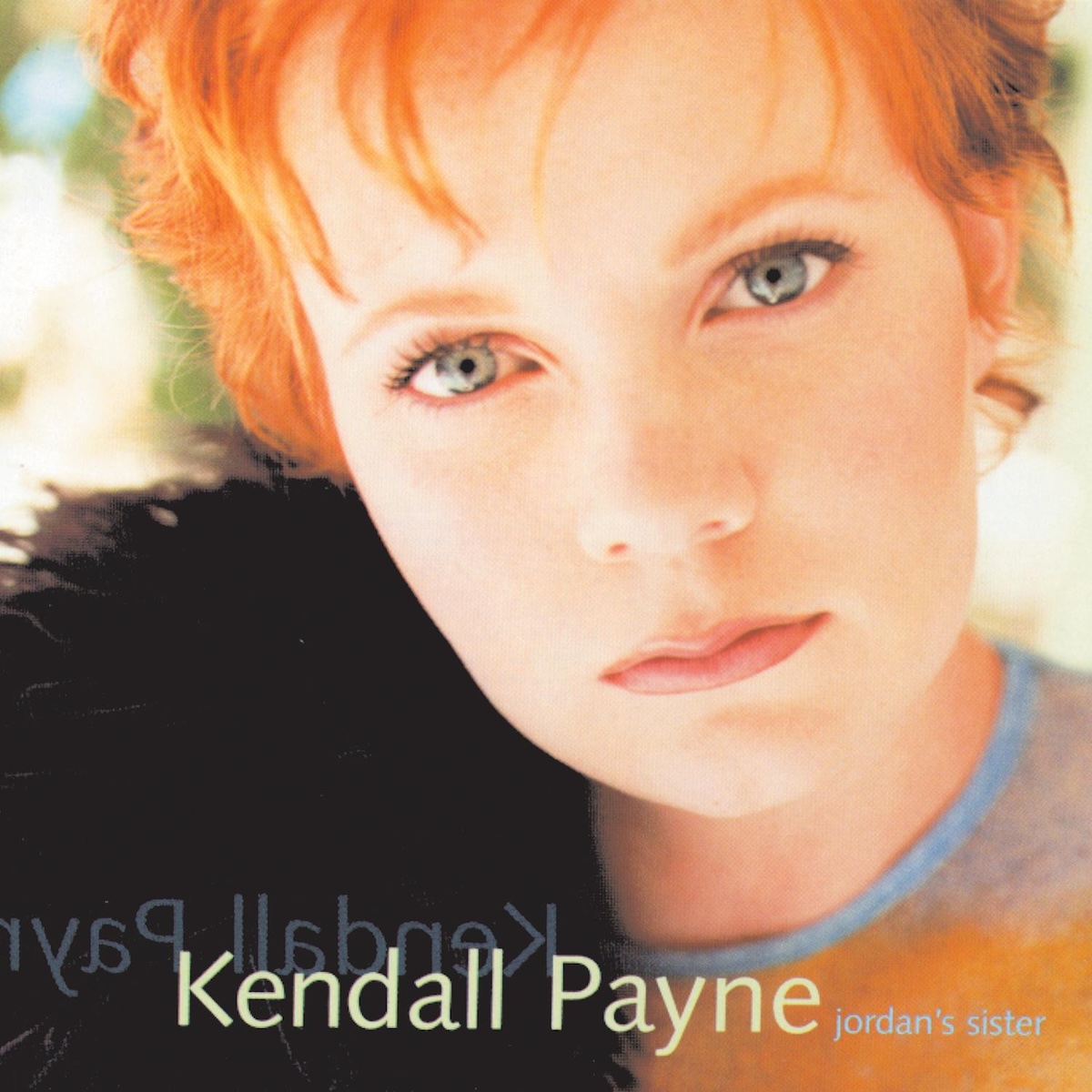 Album Art of Kendall Payne's Jordan's Sister album - A very close-up photo of a young woman. She has her head leaning slightly to the left and is looking intently into the camera with orangish-red hair that isn't too long. The background is brightly lit, probably daylight, and it looks like she's maybe wearing some fur on her right shoulder and just a thin shirt on the left shoulder. Along the bottom it says her name in a light green, and to the right of that in much smaller, light blue lowercase text the album title.