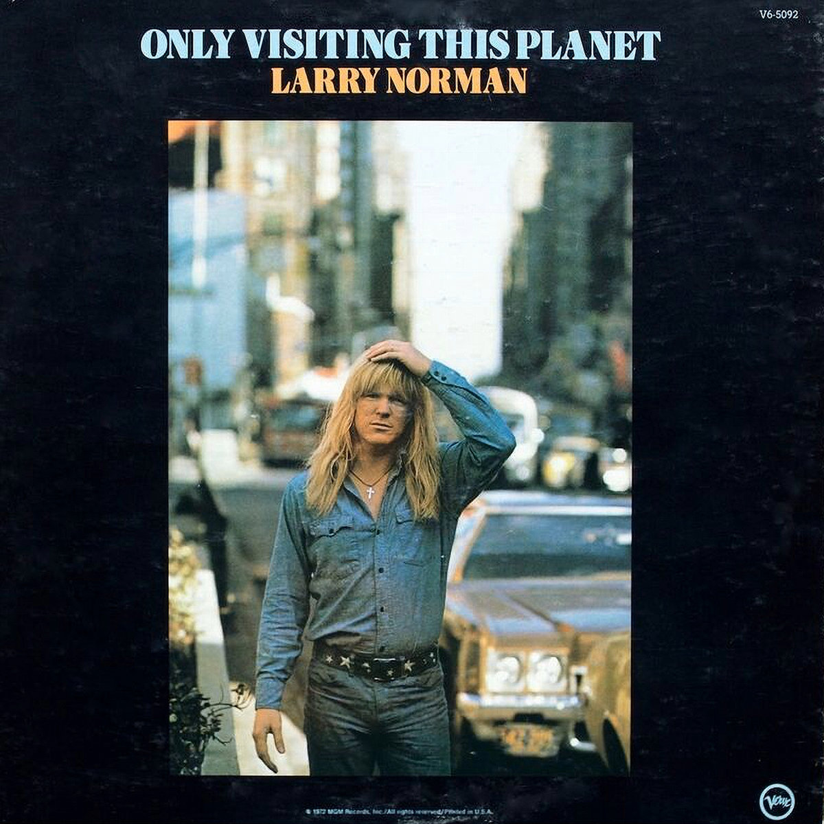 Album Art of Larry Norman's Only Visiting This Planet album - On a black background, a tall photo of a young man with long blond hair and denim jeans and a denim jacket is standing on a sidewalk in what looks to be a busy city that is blurred behind him. Above the photo, it has the album title in blue and the artist name in orange underneath it. On the edges are a small copyright and catalog number, with a Verve Records logo in the bottom right.