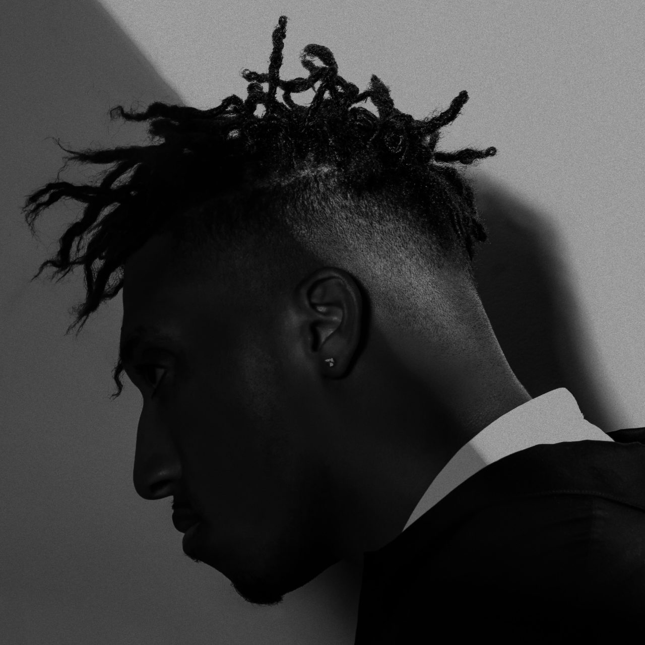 Album Art of Lecrae's All Things Work Together album - A black and white photo of a black man's neck and head, where the top right half is in light, and the bottom left is in shadow. The man is wearing a dark coat with a lighter-colored shirt and has braided hair. His face is looking down and to the left and is all in shadow.