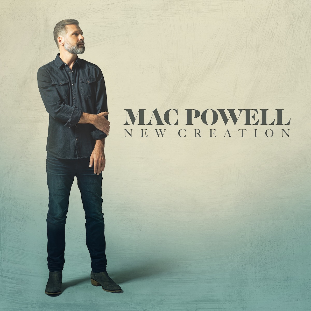 Album Art of Mac Powell's New Creation album - On a background that is more a powdery yellow at the top and more of an aqua blue at the bottom stands a middle-aged man wearing blue jeans and a matching denim shirt. He's got gray-brown hair with some spots of all gray/white and a full beard, all of them pretty short. He's looking up and to the right and has his right arm crossed over his chest to hold his left arm which is hanging down. To the right of him, there's his name in a large, dark green text, and then the album title in much smaller dark green text below.