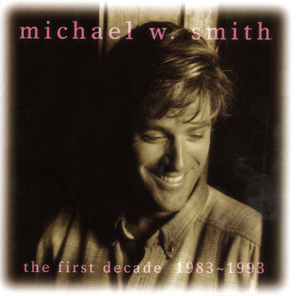 Album Art of Michael W. Smith's The First Decade album - A green-hued photo of a smiling white man with brown hair in a collared shirt from the shoulders up. Most of the background behind him is very dark. At the top in a serif font in a lighter color is the artist's name, and the album title at the bottom.