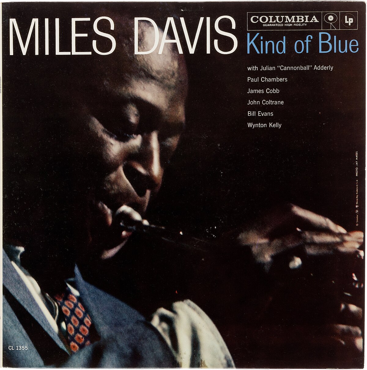 Album Art of Miles Davis's Kind Of Blue album - A photo of a black man in a navy blue suit and a tie playing a trumpet, only his upper body and the mouth of the trumpet are seen along with his hand playing the trumpet. At the top, in large print in white it says the artist name, with the title of the album in smaller blue text. Also above the album title is the Columbia Records logo and name, and below the title a list of the other players on the album.