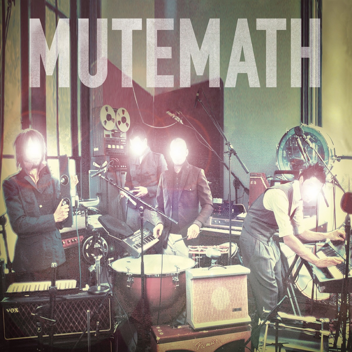 Album Art of Mutemath's self-titled album - A photo of four men in a small room amidst tons of drums, keyboards and other gear, somewhat in the midst of playing the gear but also looking at the camera, it seems. They are all wearing coats or vests and have short hair. A bright white light with maybe a bit of a red glow is emanating from where their faces should be, so their faces cannot be seen. Above the four men in the space where the walls can be seen is printed in a large, semi-transparent white print the band's name.