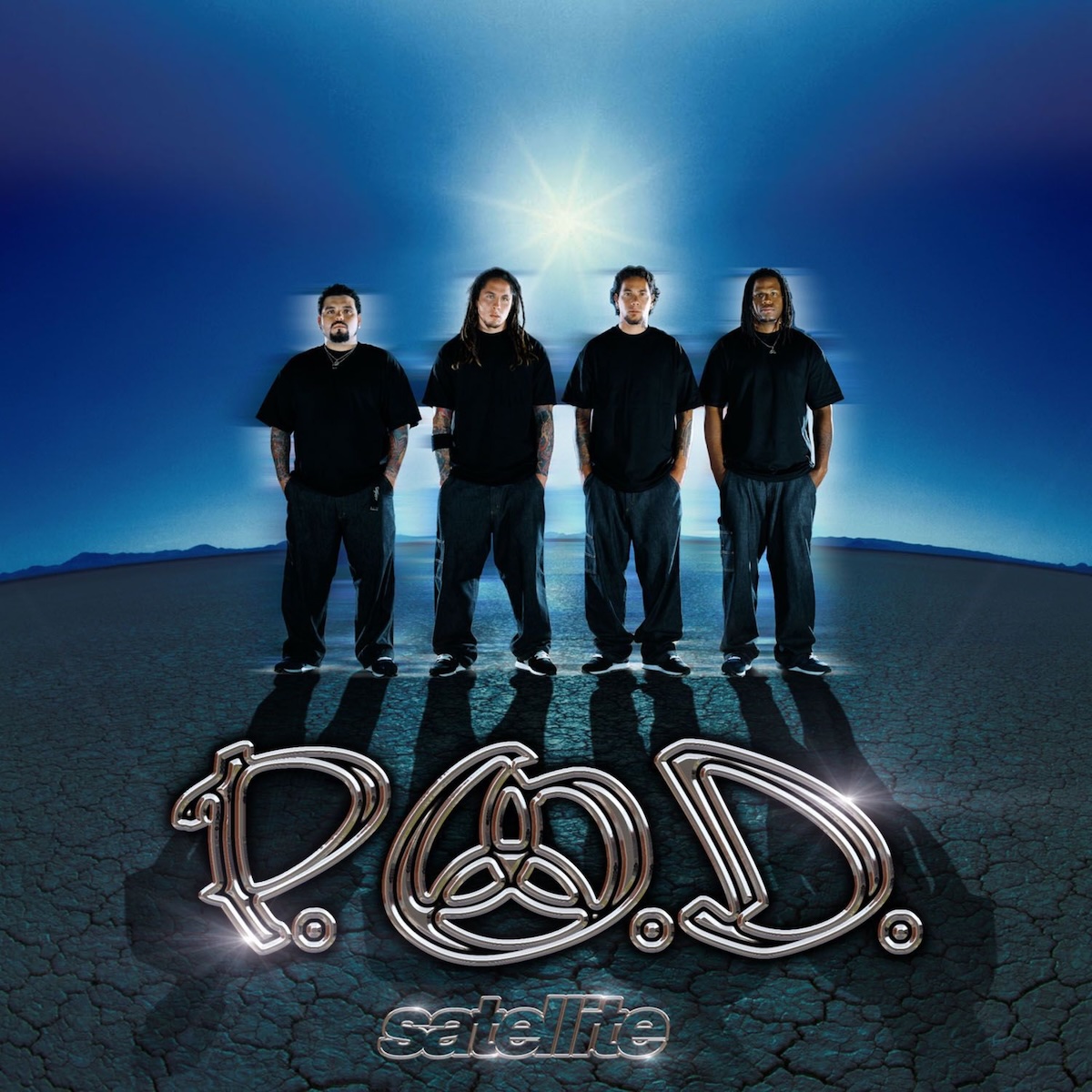 Album Art of P.O.D.'s Satellite album - A color photo of four young men in black shirts and baggy navy blue pants with black-and-white sneakers stand on a flat, desert landscape that spreads very far off to some hills way off in the background. The sky is blue and clear and the sun in shining right above their heads, putting a shadow in front of them. On the edges of each person, there's some sort of moving blur but the people are perfectly clear, so it's maybe some sort of effect or double-exposure. Printed on top of the photo is the band's word mark with a trinity symbol inside the 'O', and with an embossed, chrome metal look. In smaller text, the word 'satellite' is outlined in silver chrome metal.