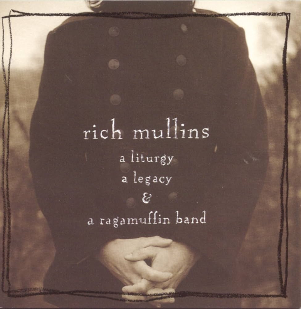 Album Art of Rich Mullins's A Liturgy, A Legacy & A Ragamuffin Band album - A man wearing a big, thick brown coat with buttons down both sides is only shown from neck to waist with hands clasped in front of the waist and behind looks like a field or landscape with some bushes or trees in spots. In a hand-written-looking font, the band name is in the center with the album name below in white. Around the edge is a hand-drawn border.