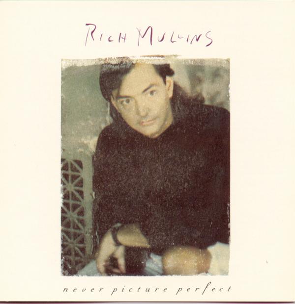 Album Art of Rich Mullins's Never Picture Perfect album - On a creamy white background, a color photo of a middle-aged man sitting on a chair in shorts and a black shirt. He's looking to the right of the camera with a very serious stare. The photo is very grainy and has a rough, kinda painted edge. Above the photo, written in a dark red pen is the artist's name. And below in a dark red italics serif font in all lowercase is the album title.