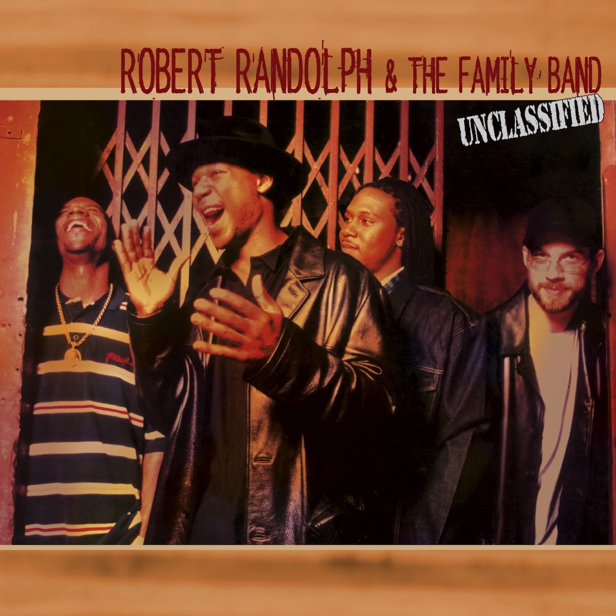 Album Art of Robert Randolph And The Family Band's Unclassified album - The top and bottom have a golden brown, blurry background. In the middle, a photo of four men standing in front of some sort of metal gate. The one in front is looking to the left side of the frame and clearly excited and exclaiming about something, with his hand about to clap together. He's also wearing a black leather jacket and a black brimmed hat. At the top above the photo, it has the band's name printed in a reddish brown, and on top of the upper right corner of the photo is printed the words 'Unclassified' in uppercase in a black, stamp-like font.