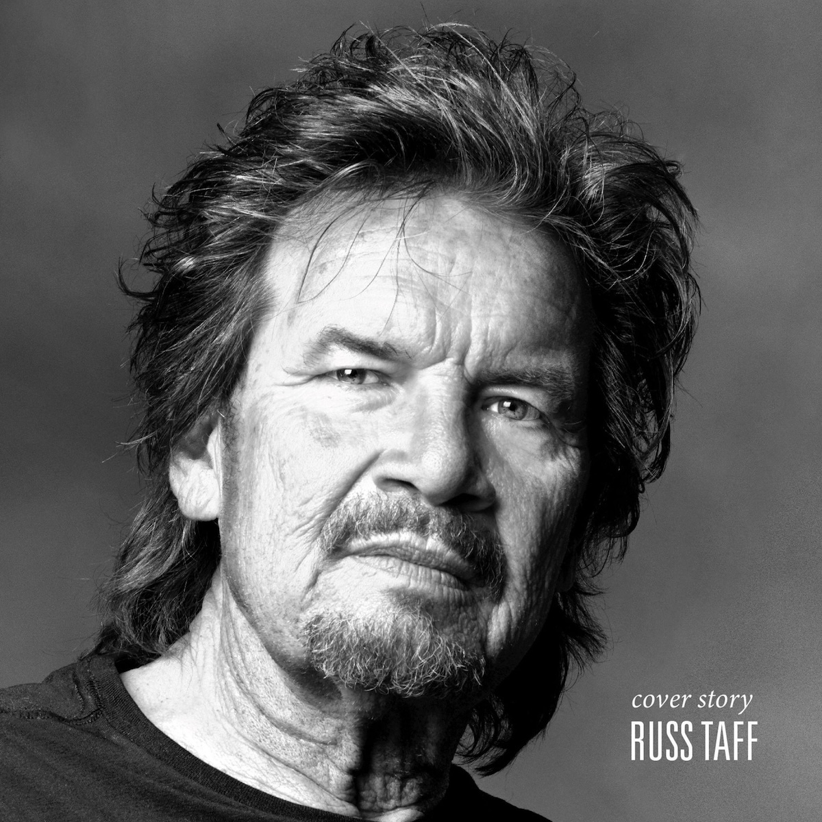 Album Art of Russ Taff's Cover Story album - A black and white photo of an older white man with shoulder-length dark but graying hair slicked back, a beard and mustache, wearing a dark T-shirt, on a gray background. In the bottom right is the album title in lowercase in a script font, and the artist's name in a bigger, blocky font in white.