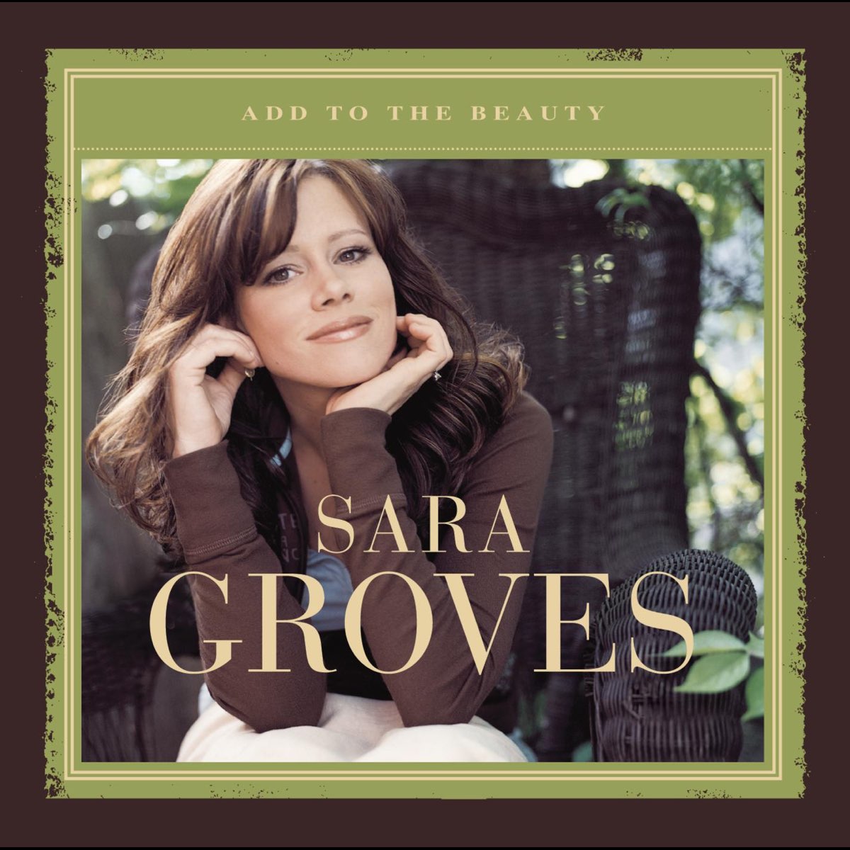 Album Art of Sara Groves's Add To The Beauty album - In a brown wicker chair with light filtering through trees and leaves in the background, the artist, a white woman with long, brown hair, leans toward the camera. In front of her is printed her name, 'Sara Groves'. Around the photo is a green border, and at the top it has the album title. Around that green border is a larger brown border.