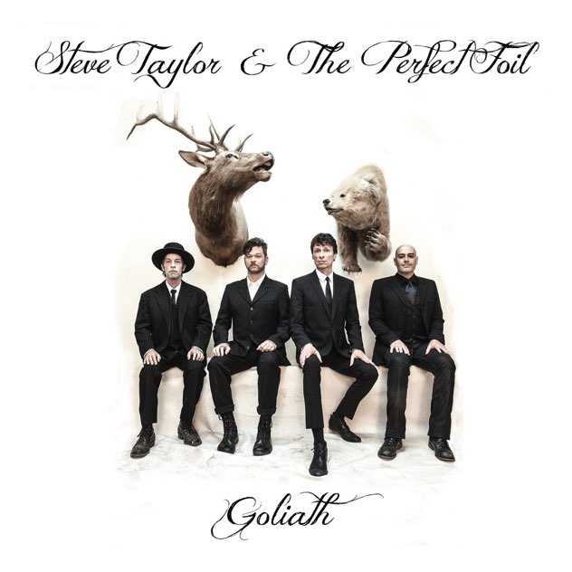 Album Art of Steve Taylor And The Perfect Foil's Goliath album - Four men in black suits are sitting on a white background with a deer head and bear head behind them. Above them, in a flowing script, is the band name and below is the album title.