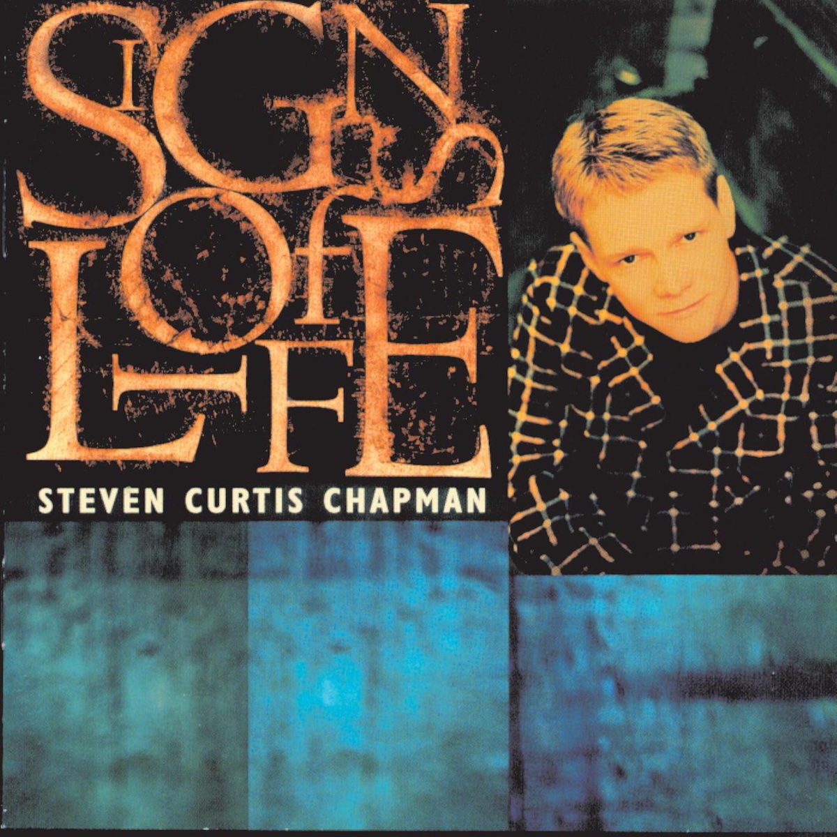 Album Art of Steven Curtis Chapman's Signs Of Life album - In the top left and stretching to nearly half the cover area, the letters of the album title are set on a black background in orange in various orientations. Some letters are smaller than others and some letters on their sides or sitting inside of other letters, so they're kinda jumbled up a bit. Below that, the artist's name is printed in small text. To the right of this main are is a portrait photo of a white man with light-colored, short hair wearing a black suit with large orange stripes. At the bottom is a blue texture of some sort.