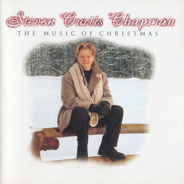 Album Art of Steven Curtis Chapman's The Music Of Christmas album - On a white background, the artist's name is in a white, flowing script with a red glow around them. And the album title is below that in small black text. Below that is a photo of the artist, a young, white man with blonde hair parted right in the center of his head, wearing a jacket, a scarf and gloves, sitting on a wooden fence with a snowy clearing behind and a forest in the background.