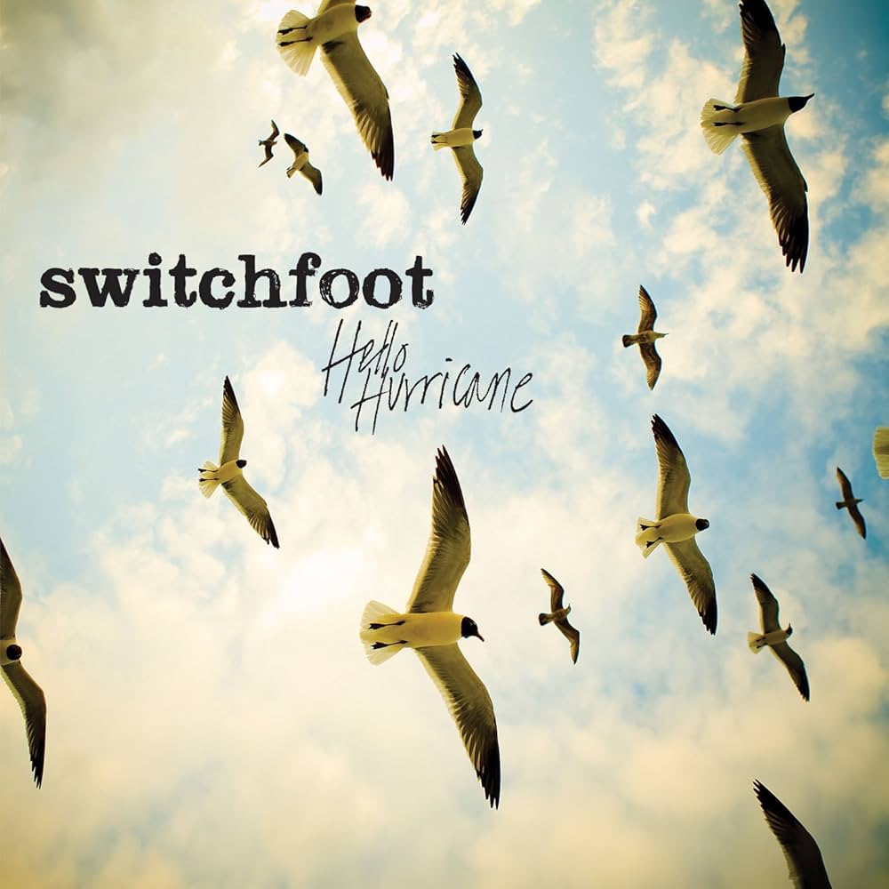 Album Art of Switchfoot's Hello Hurricane album - looking straight up, a partly cloudy sky with sun filtering through the clouds and a flock of birds flying in the foreground. The words 'Switchfoot' are printed in a large, blocky font and the words 'Hello Hurricane' are in a thin script.