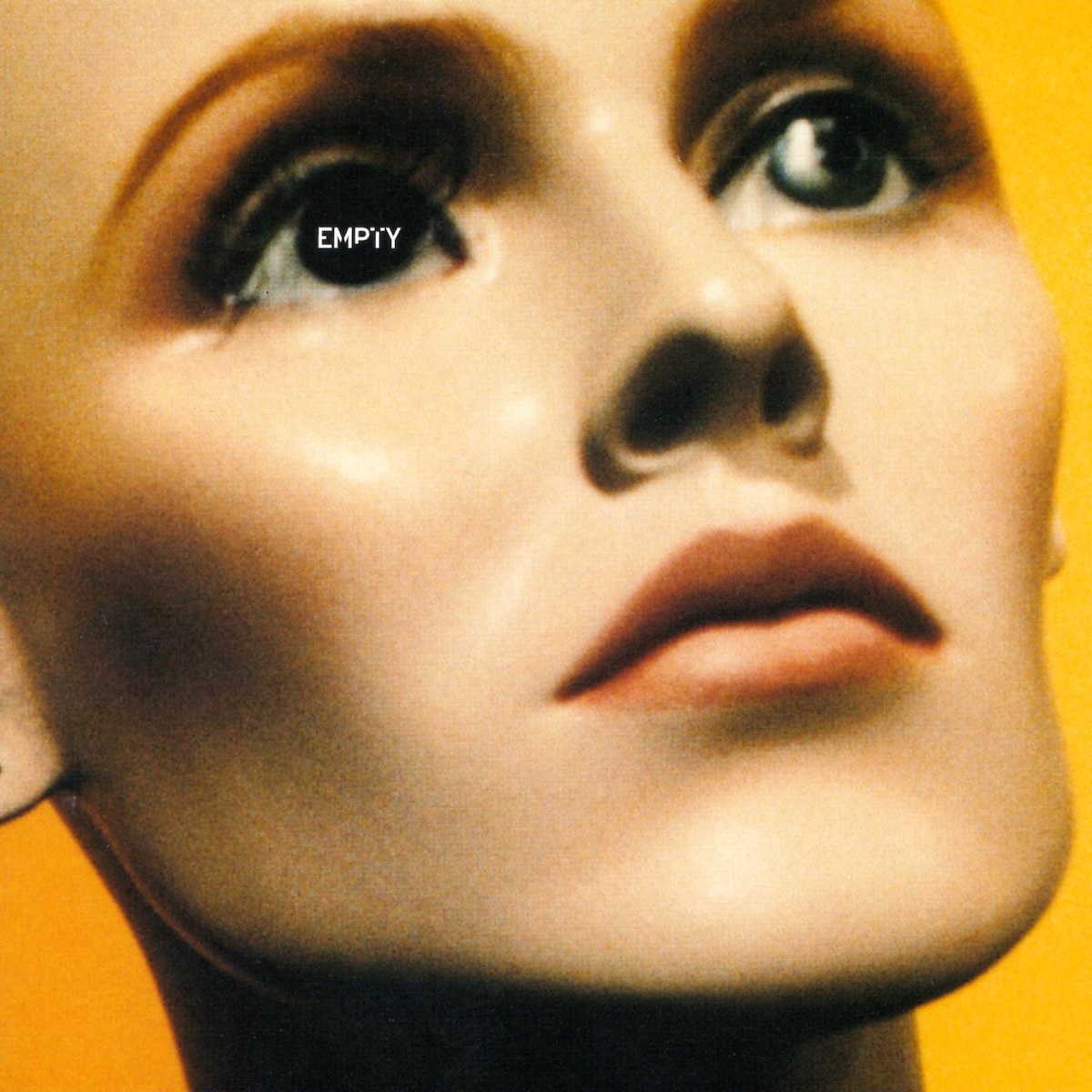 Album Art of Tait's Empty album - A close-up photo of a female mannequin's head on a bright yellow background. The image is a bit blurry and printed above the mannequin's left eye is the word 'empty' in capital letters in white. The mannequin has a very defined cheekbone and seems to be looking above and beyond the camera.