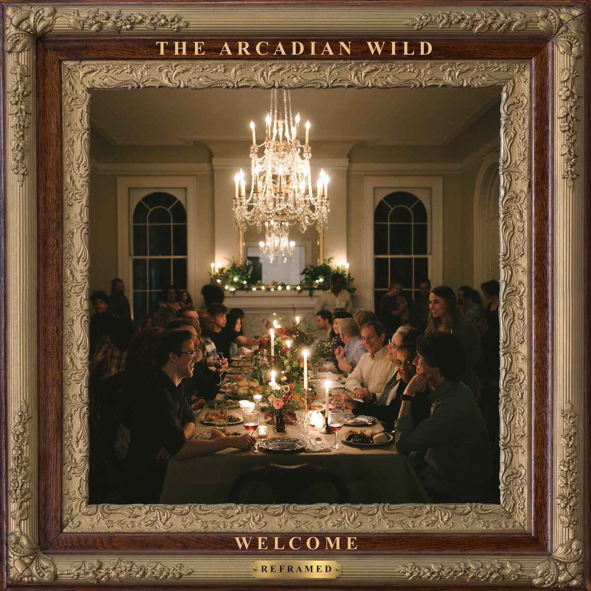 Album Art of The Arcadian Wild's Welcome (Reframed) album - In the middle, a beautiful photo of a large dining room with a large table with a tablecloth, candles, flowers and food in the middle as well as food on plates. About 15 people are sitting on chairs on the side of the table. Around the table lots of people are standing around as well. Above the table is a large chandelier. Beyond the table is a large mantle with a mirror above it and large windows on both sides.</body></html>