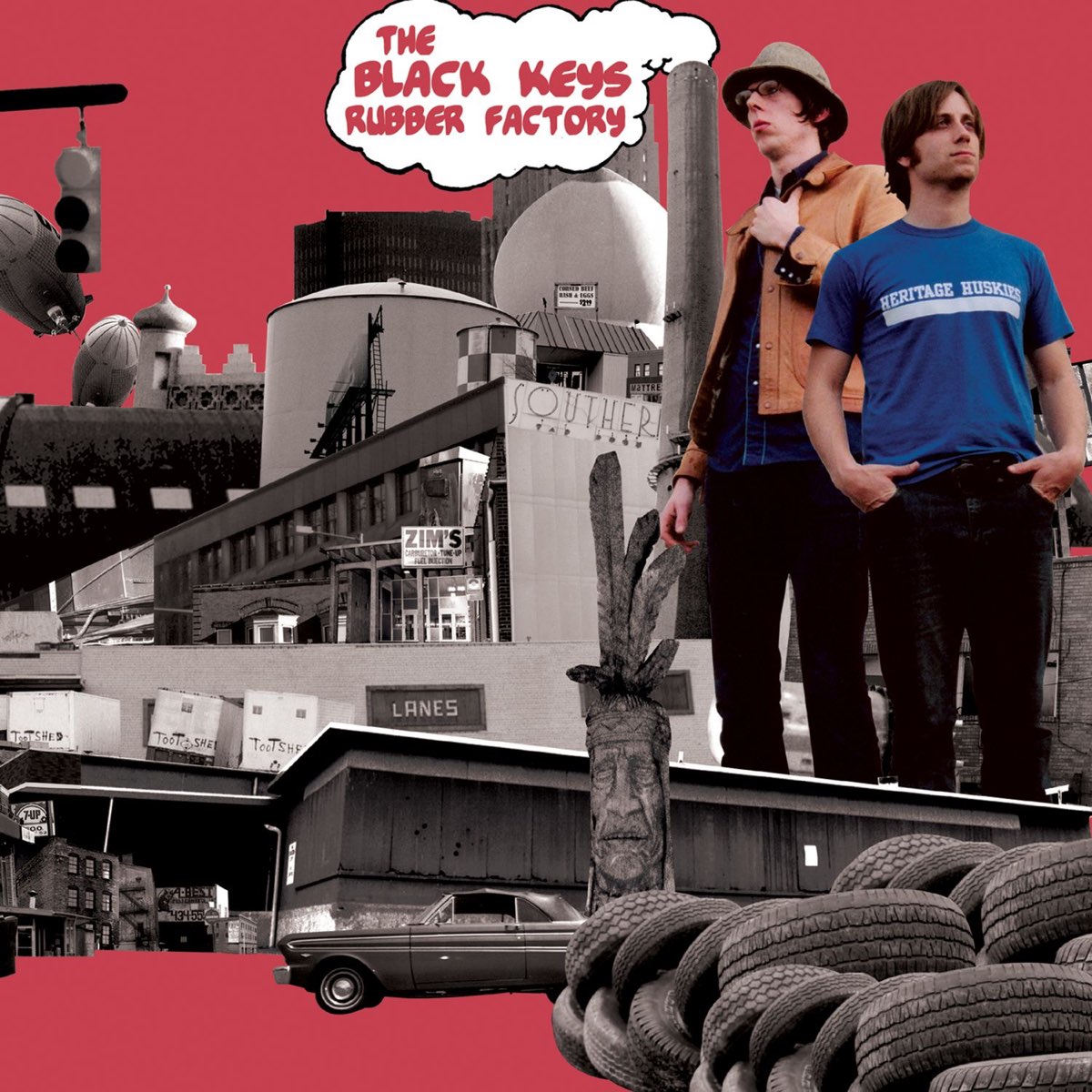 Album Art of The Black Keys's Rubber Factory album - On a red background with a hint of pink in the hue, a bunch of photos are cut together on top of each other. Black and white photos of cityscapes, industrial storage tanks, loading docks, and a few different shots of factories are layered on top of each other, and in the front is a pile of tires for cars and an old sedan behind it. In the middle is a tall set of smokestacks, and out of the right one is drawn a white cloud with a black border, and inside it is written the band name and album title in the same red in a hand-drawn font. To the right of the smokestack and nearly as tall is a cut-out, color photo of the two band members, both white men, one with black hair, glasses and a bucket hat, the other with brown hair.