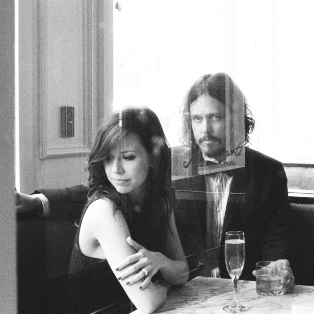 Album Art of The Civil Wars's Barton Hollow album - A black and white photo of two young white people, on the right a man with curly hair, a beard and mustache in a suit coat with a bowtie, and on the left, a woman with darker, long hair and a sleeveless dark top. They are sitting in a corner booth with a marble tabletop sitting in front of them and glasses of water on the table.</body></html>