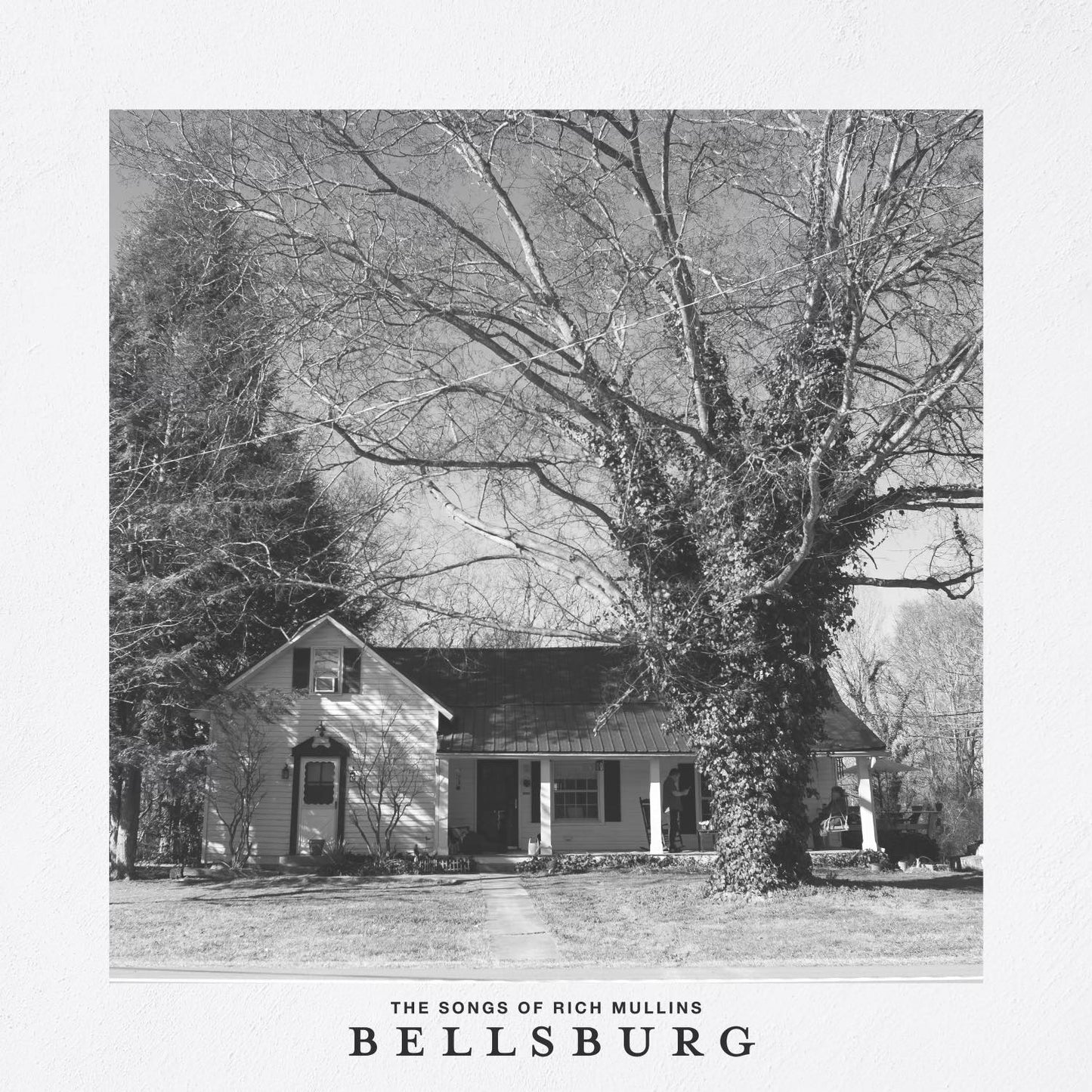 Album Art of The Bellsburg Sessions album - In the middle, a black-and-white photo of a small, simple house with a large tree in the right side of the front yard. The house has a covered porch behind the tree on the right side. Around the photo is a large, nearly-white gray border, and on the bottom it says 'Bellsburg' in large type and 'The Songs of Rich Mullins' below it.